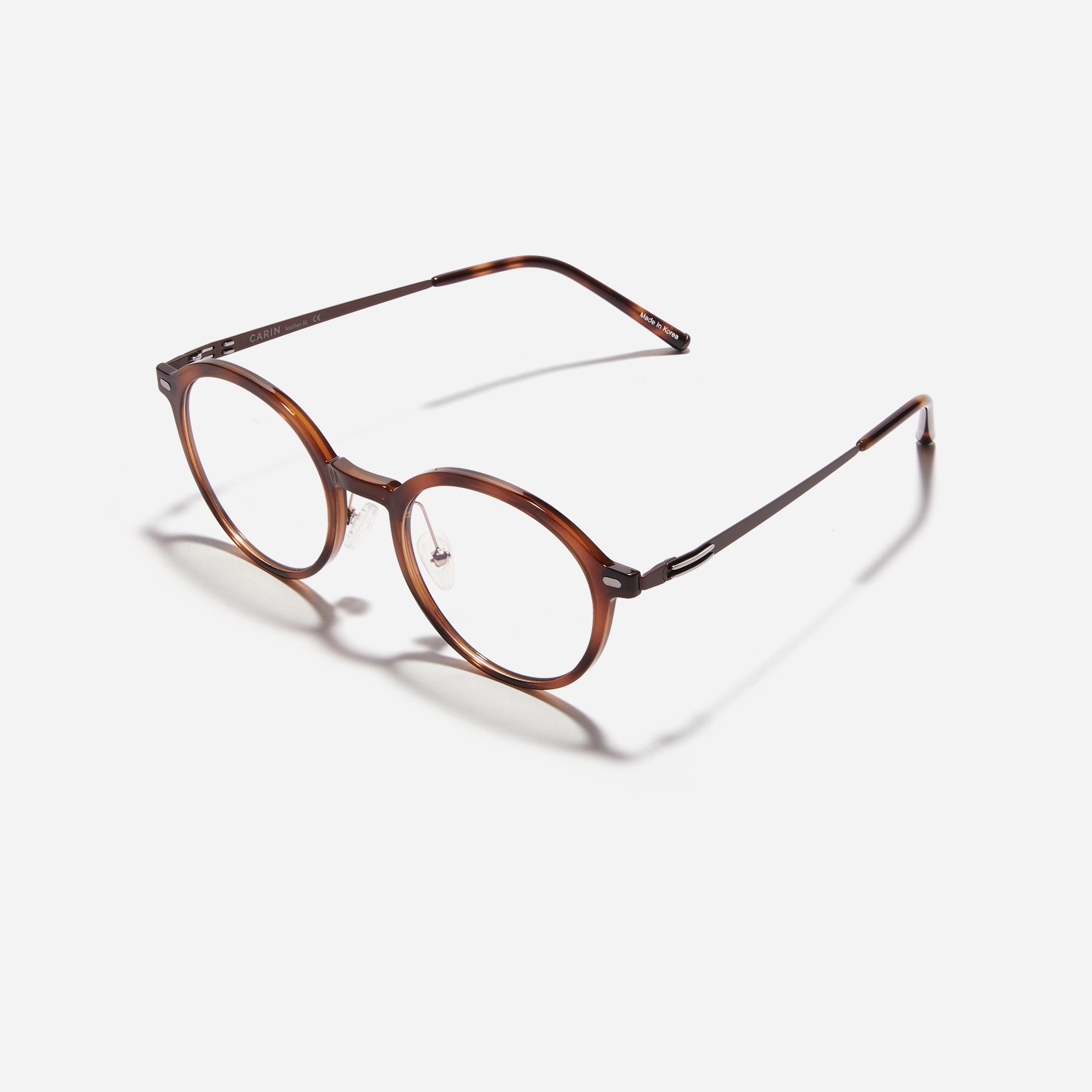 Round-shaped combination eyeglasses from CARIN's 'Feather Fit' line. Their combination frame seamlessly blends bio-plastic and titanium, utilizing advanced injection molding technology, often seen in the manufacturing of cell phones and watches.